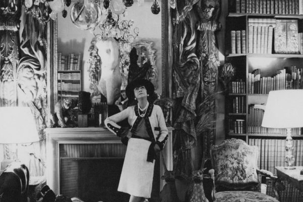 French fashion designer, Coco Chanel, standing, in her Paris apartment, with her back to a mantle fireplace, with a large mirror above, looking up at a chandelier *** Local Caption *** Coco Chanel;