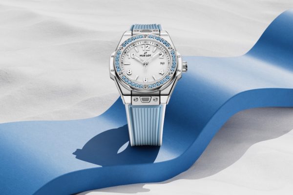 La montre Big Bang One Click Joyful Blue de Hublot sertie de topazes bleues est photographiée sur un tapis bleu et du sable blanc ©Hublot
