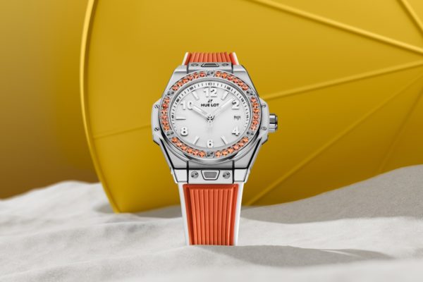 La montre Joyful Orange, sertie de saphirs oranges, est photograpiée dans le sable devant un élément jaune.